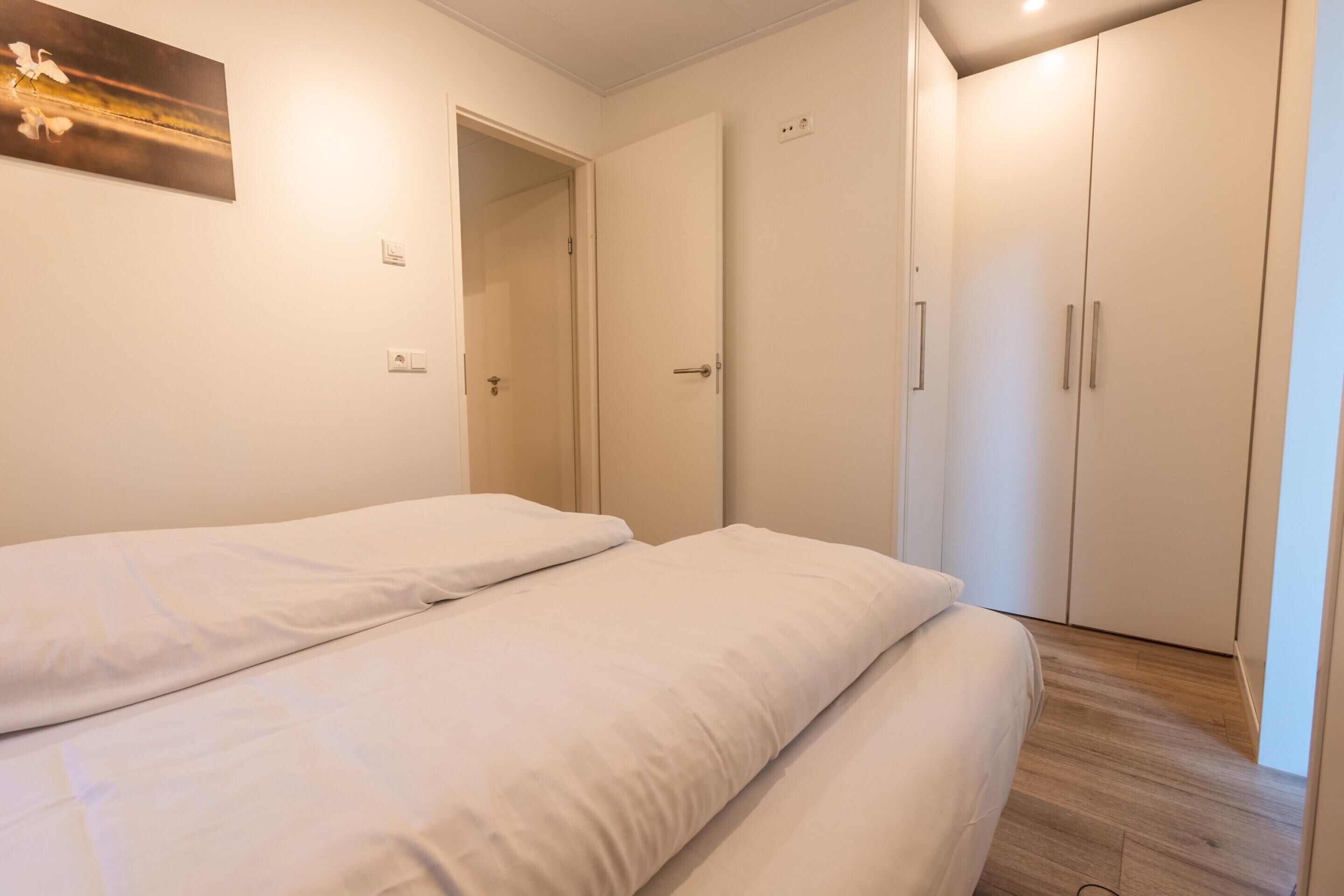 A bedroom with two beds, a wardrobe, and a door leading to another room.