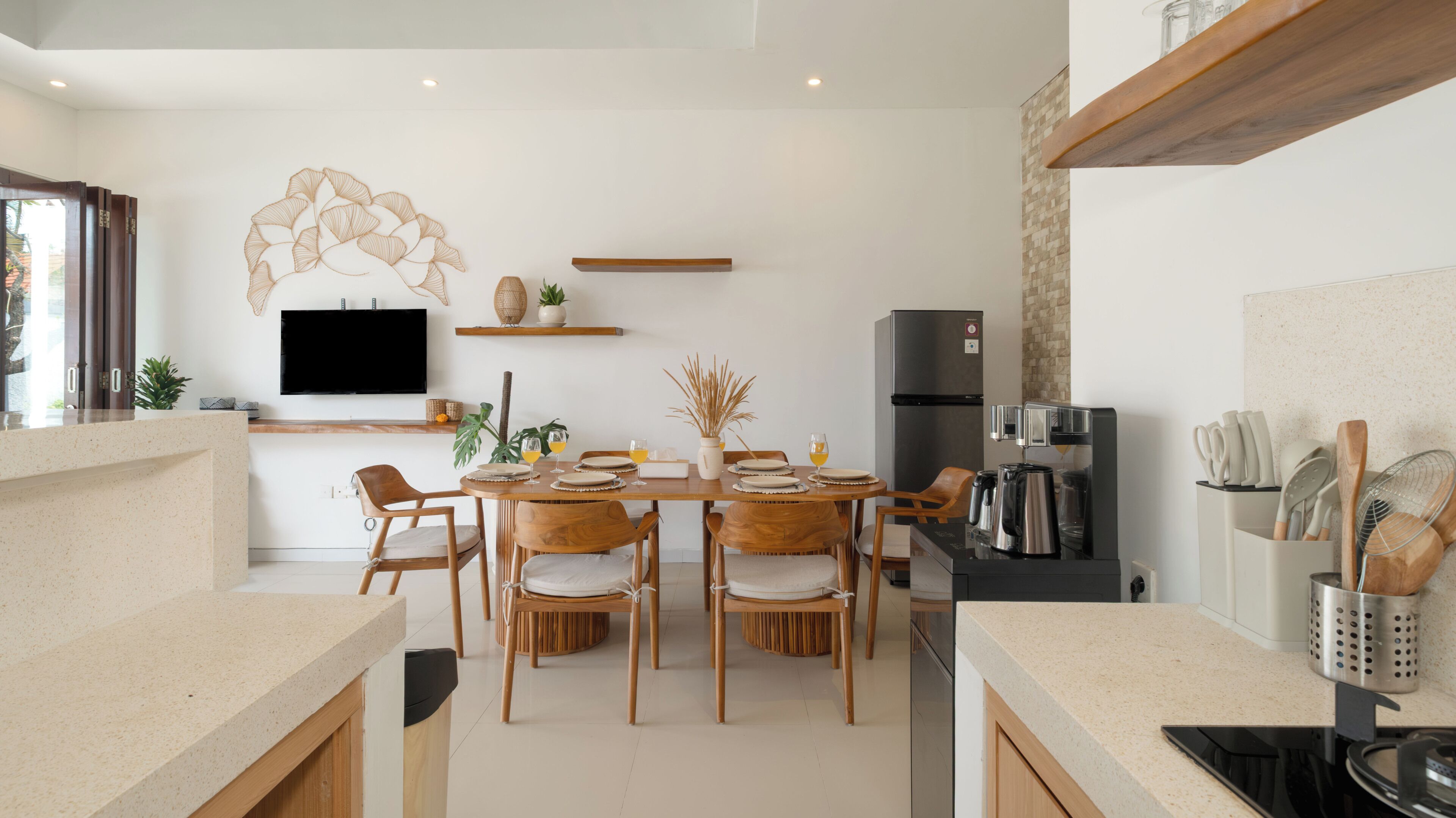 A modern kitchen with a dining area, wooden furniture, a flat-screen TV, and a built-in oven.
