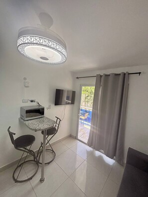 Una habitación pequeña y moderna con una mesa de comedor, sillas, un microondas, un televisor y una lámpara en el techo.