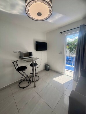 Una habitación pequeña con una televisión montada en la pared, un microondas, una mesita con una silla y un cristalero corredizo que da a un área exterior.
