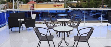 Een terras buiten met tafels en stoelen, uitzicht op de straat en een gebouw met een bord.