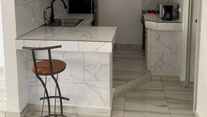 A compact kitchen with white cabinets, a marble countertop island, a bar stool, and a coffee machine. - Chambre Double #300 de l'Hôtel Legendario (Sosúa)