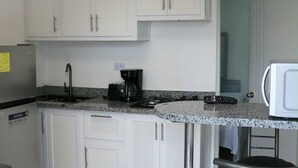 Una cocina moderna con armarios blancos, encimera de granito, refrigerador de acero inoxidable, cafetera y microondas.
