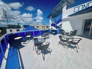Una terraza en la azotea con asientos al aire libre, una carpa azul y un edificio con un letrero que dice 'CON'.