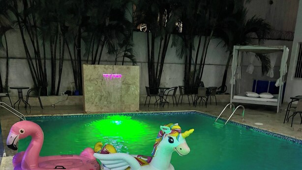 Una piscina con juguetes inflables, un borde de piedra y un área de descanso con sillas y una mesa.