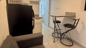 A compact kitchen with white cabinets, a black refrigerator, a dining table with two chairs, and a ceiling light fixture. - nouveau condo près de tout plage épicerie 203 (Sosúa)