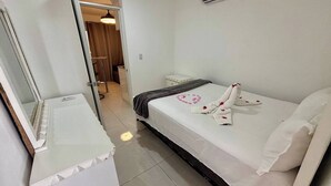 Una habitación de hotel con una cama, una mesita de noche pequeña, un espejo y un equipo de aire acondicionado.