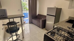 A compact kitchen with a gas stove, a refrigerator, a dining table with a chair, and a ceiling light fixture. - Condo, neuf, balcon en plein coeur de Sosua 204 (Sosúa)