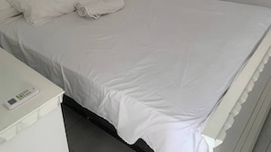 Una cama blanca con almohadas, una mesita de noche y un aire acondicionado de pared.