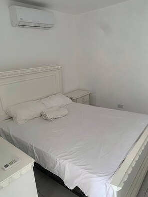 Ein weißes Bett mit Kissen, ein Nachttisch und eine wandmontierte Klimaanlage.