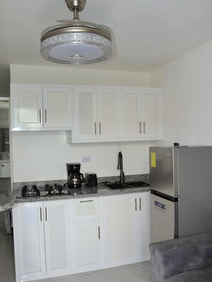 A kitchen with white cabinets, a stainless steel refrigerator, a coffee maker, and a gas stove. - condo neuf a sosua près de tout 304 (Sosúa)
