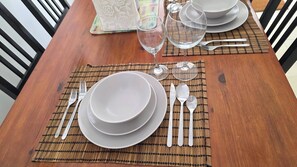 Une table de salle à manger en bois, mise avec des assiettes blanches, des bols, des couverts et un verre d’eau.