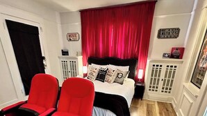 Una camera da letto con un letto, due sedie rosse, una tenda rossa e un pavimento in legno.