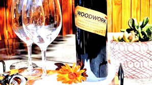 Una bottiglia di vino Woodwork, due bicchieri, un cartello con la scritta 'Refresh' e un cesto decorato con fiori.