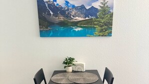 A dining area with a table, four chairs, a plant, and a painting of a mountain landscape. - Near Airport, Hospital, MidTown, 58” TV - Apt 254 (Reno)