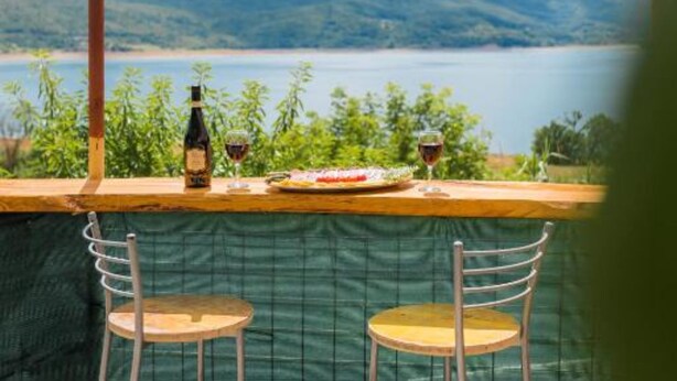 Un coin repas offrant une vue sur un lac et des montagnes, avec une table, des chaises et une bouteille de vin.