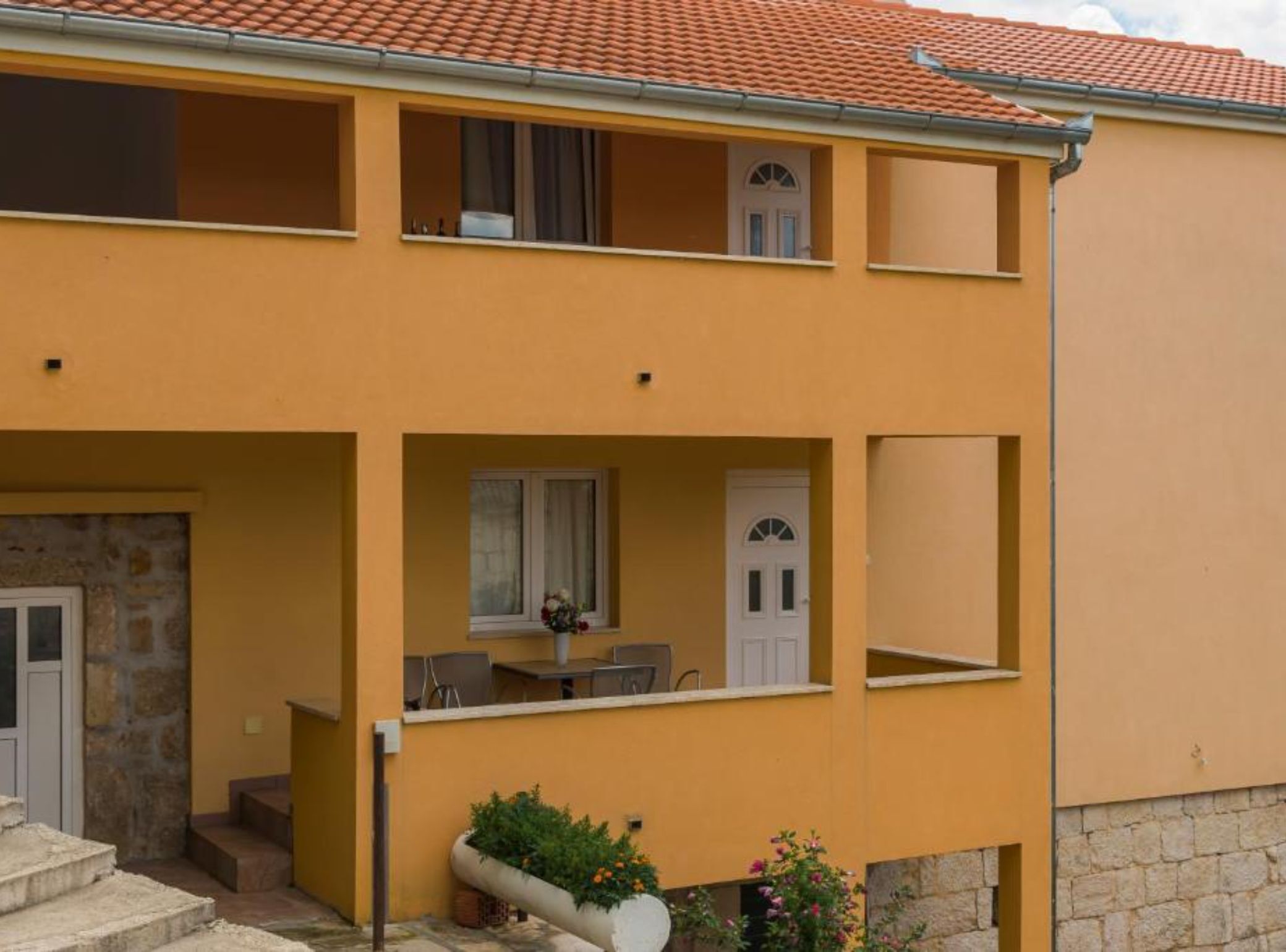 A two-story building with a yellow facade, a stone base, and a tiled roof.