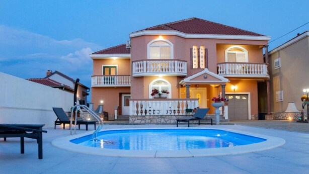 A two-story house with a swimming pool, balconies, and outdoor seating.