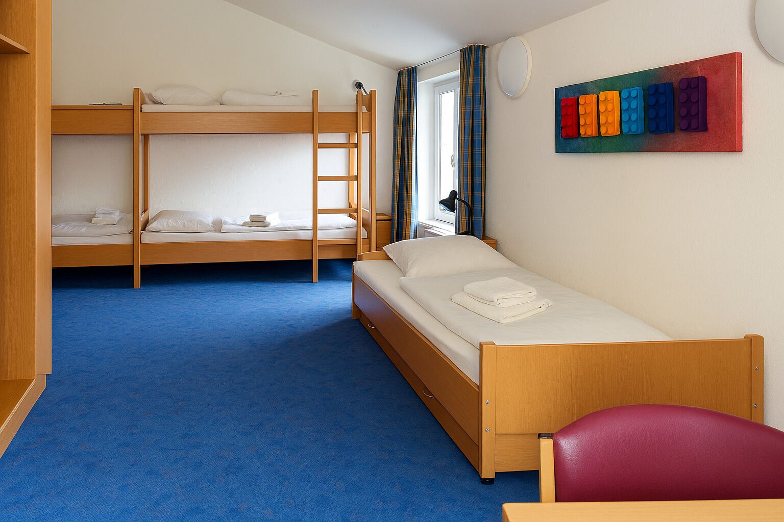 A room with bunk beds, a single bed, a red chair, and a colorful wall art piece.