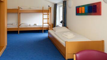 A room with bunk beds, a single bed, a red chair, and a colorful wall art piece.