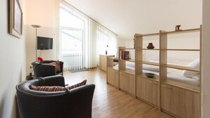 Une pièce comprenant un canapé, un téléviseur, un meuble en bois avec des étagères et une fenêtre avec des stores.