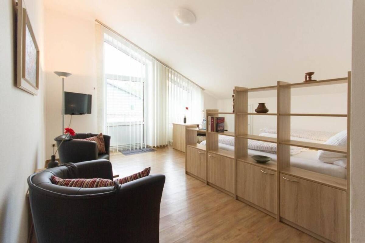 A room with a sofa, a TV, a wooden cabinet with shelves, and a window with blinds.