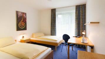 A hotel room with two beds, a desk, a chair, a desk lamp, a telephone, and a painting on the wall.