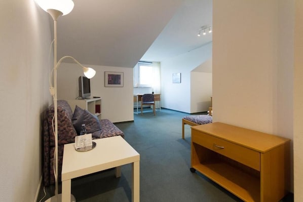 Ein Zimmer mit Schreibtisch, Stuhl, Lampe und einem kleinen Holzschrank.
