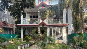 A two-story building with a balcony, surrounded by a garden with various plants and a paved walkway. - Villa The Kinara Resort (Kihim)