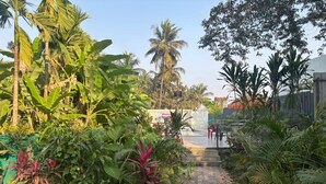 A paved pathway leading to a seating area with chairs, surrounded by lush tropical vegetation and palm trees. - Villa The Kinara Resort (Kihim)