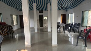 A spacious room with a high ceiling, a marble column, a dining area with chairs, and a bed with a striped blanket. - Villa The Kinara Resort (Kihim)