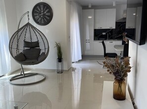 A modern living room with a hanging chair, a clock, a potted plant, and a vase with dried flowers. - Apartment Rogoznica (Rogoznica)