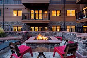 An outdoor patio area with a fire pit, seating, and a stone wall. - Condo + Ski Shuttle + Pool + Spa Access | Mountain Dream at Frontgate (Avon)