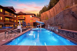 A swimming pool with a slide, lounge chairs, and a building with balconies. - Condo + Ski Shuttle + Pool + Spa Access | Mountain Dream at Frontgate (Avon)
