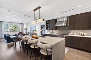 A modern kitchen with a central island, bar stools, and a dining area with a sofa and table. - Condo + Ski Shuttle + Pool + Spa Access | Mountain Dream at Frontgate (Avon)