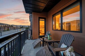 A balcony with wooden furniture, a view of a sunset, and a building in the background. - Condo + Ski Shuttle + Pool + Spa Access | Mountain Dream at Frontgate (Avon)