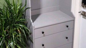 Ein grauer Stauraum mit einem Regal und drei Schubladen, einer Blumentopf-Pflanze und einer Tür mit Griff.