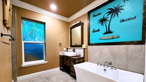 A bathroom with a large bathtub, a window with a view, a mirror, and a wall with a tropical-themed artwork. - Tropical Spa Studio, Jacuzzi, Kitchen, Sparks (Sparks)