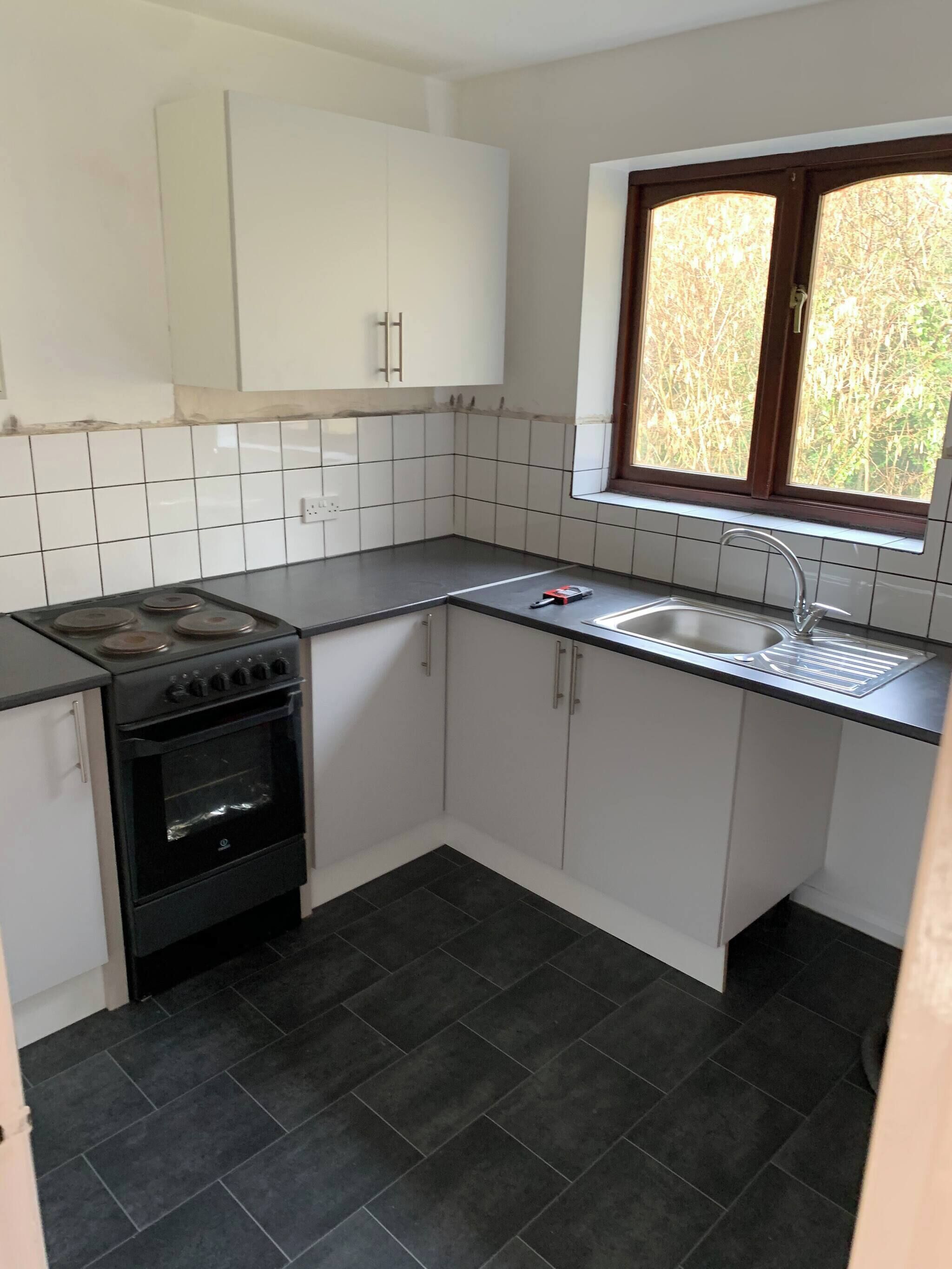 A compact kitchen with white cabinets, a black stove, a sink, and a window with a view of trees.