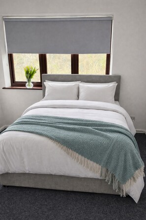 Un dormitorio con cama, ventana con vistas y un florero con flores en el alféizar.