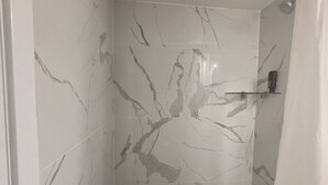 Ein Badezimmer mit weißen Marmorfliesen und einer Duschkabine.