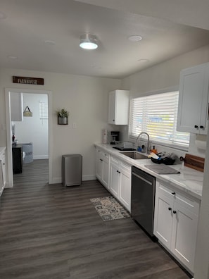A modern kitchen with white cabinets, a stainless steel dishwasher, and a window with blinds. - Modern Las Vegas Retreat, Spacious 4-bedroom house in a pleasant neighborhood (Las Vegas)
