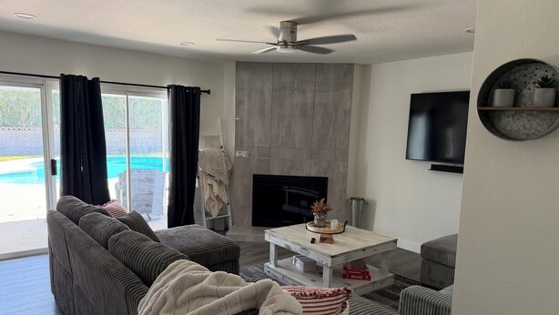 Ein modernes Wohnzimmer mit Ecksofa, Kamin, Flachbildfernseher und Blick auf einen Pool.
