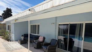 Ein überdachter Patio-Bereich mit Gartenmöbeln, eine Glasschiebetür zum Pool und eine auf dem Dach montierte Überwachungskamera.