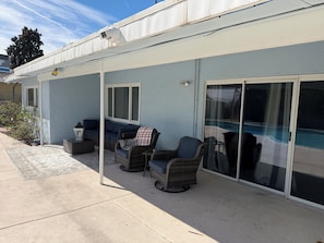A covered patio area with outdoor furniture, a sliding glass door leading to a pool, and a security camera mounted on the roof. - Modern Las Vegas Retreat, Spacious 4-bedroom house in a pleasant neighborhood (Las Vegas)
