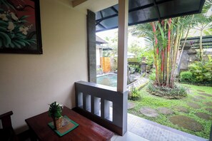 A wooden dining table with a pineapple centerpiece, a framed painting on the wall, and a view of a garden with bamboo plants and a stone pathway. - Ubud Private Pool Villa Tropical Hideaway with Ricefield View (Ubud)