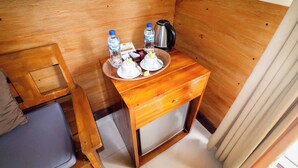 Een kleine keuken met een houten aanrecht, een waterkoker, waterflesjes, een koffiezetapparaat en een kleine koelkast.