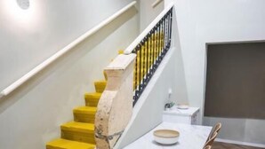 Ein Essbereich mit einem Marmortisch, Korbstühlen und einer Treppe mit gelben Stufen.