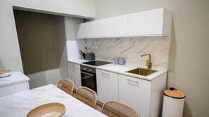 Eine kompakte Küche mit weißen Schränken, einer Marmorarbeitsplatte, einem Einbauofen und einem Spülbecken mit goldfarbenem Wasserhahn.