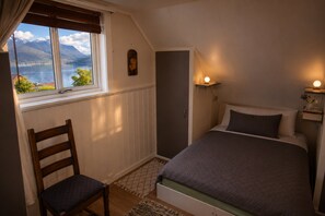 A bedroom with a bed, a chair, a window with a view of mountains, and a wall-mounted shelf with a light. - Casa Hauge Fjord View (Sandane)